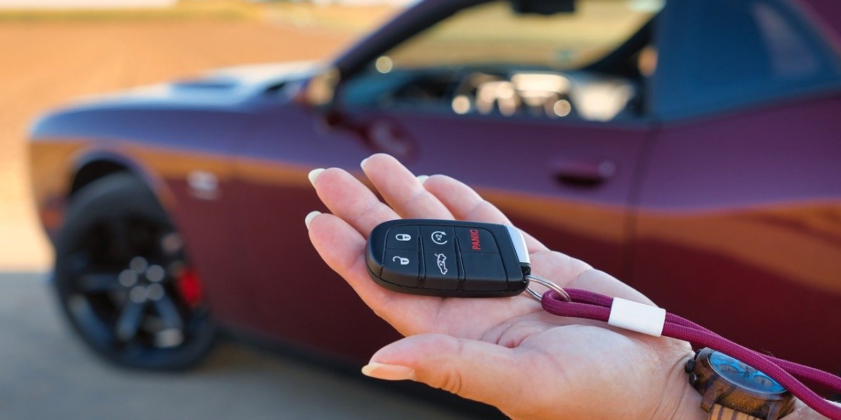 A hand holds a car key fob with a red lanyard. In the background, a maroon sports car is parked in a sunlit area, emphasizing a sense of ownership and freedom.